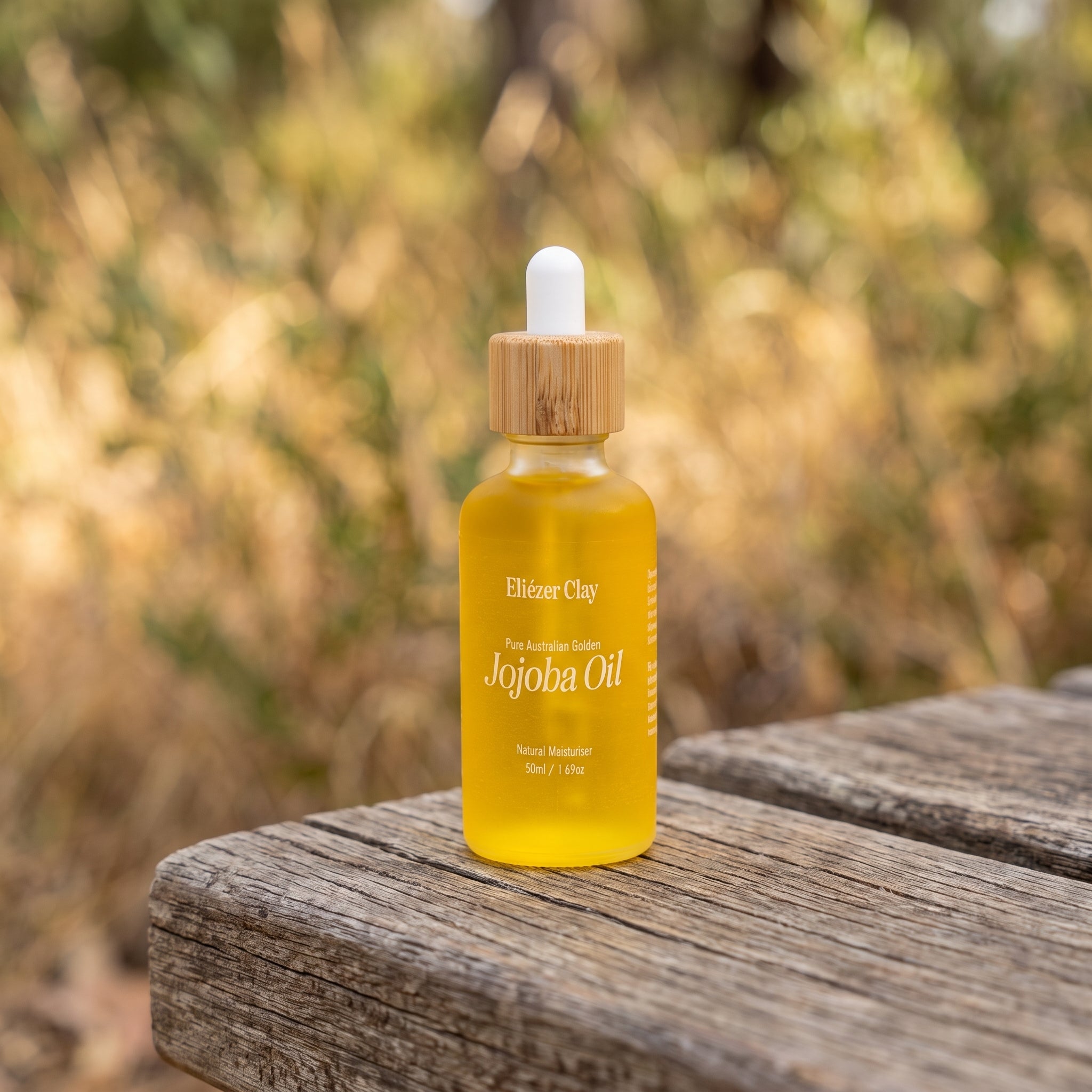 Bottle of Eliézer Clay pure Australian golden jojoba oil on a rustic timber bench outdoors