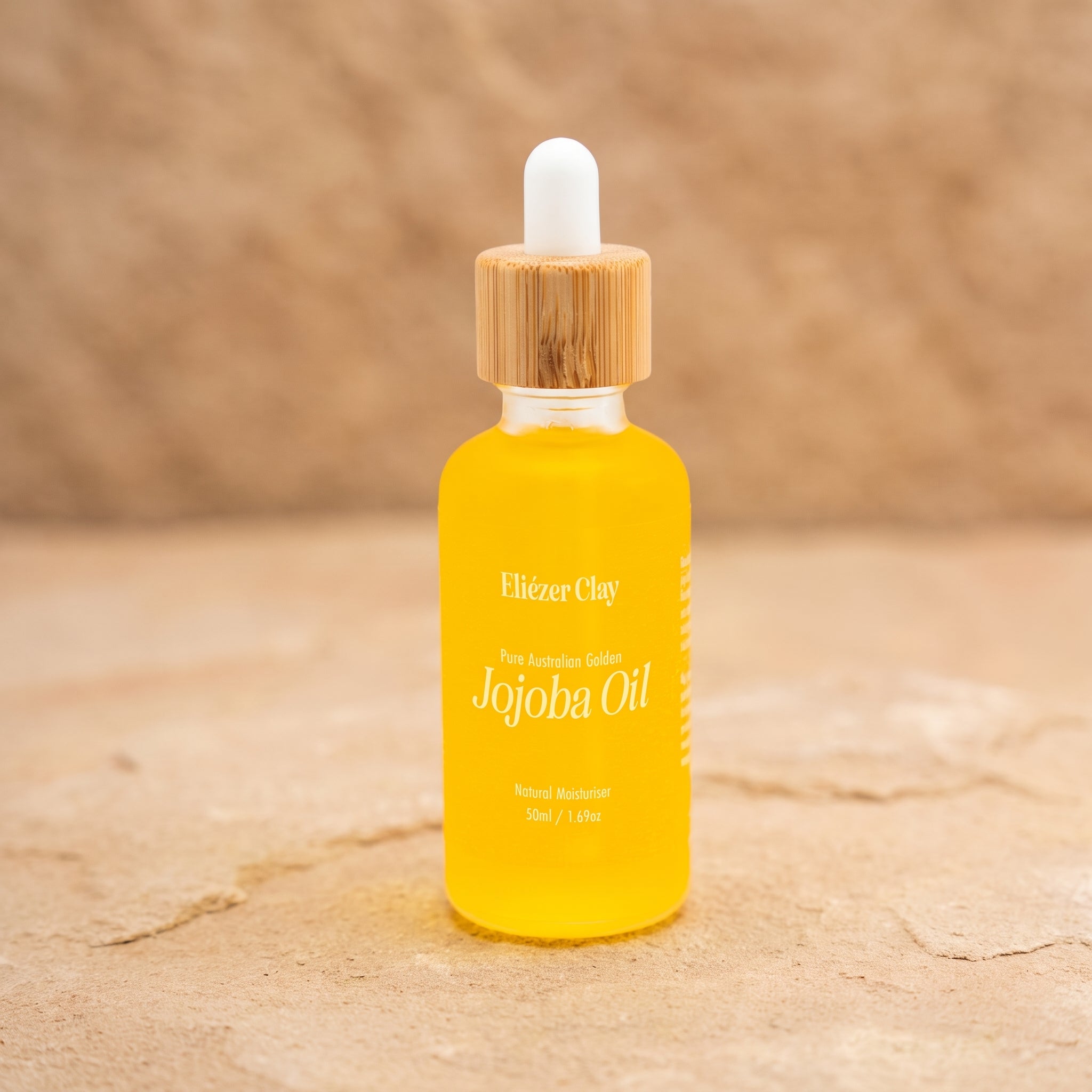 Bottle of Eliézer Clay pure Australian golden jojoba oil on a matte sandstone surface