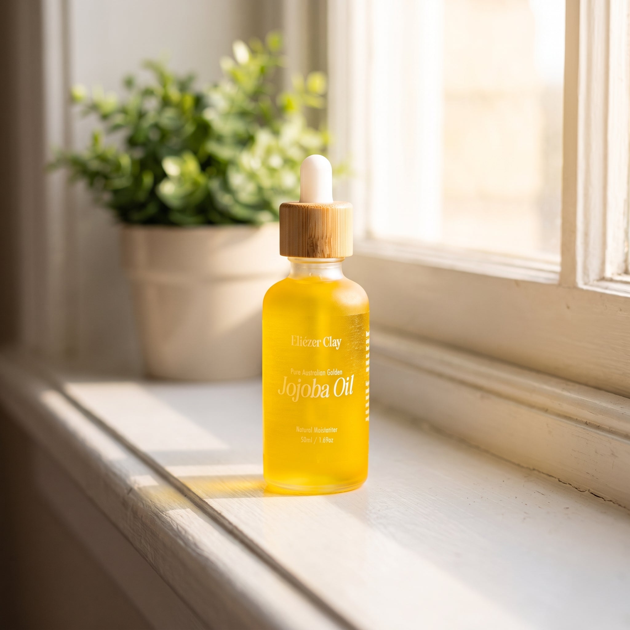 Bottle of Eliézer Clay pure Australian golden jojoba oil on a windowsill beside a green plant
