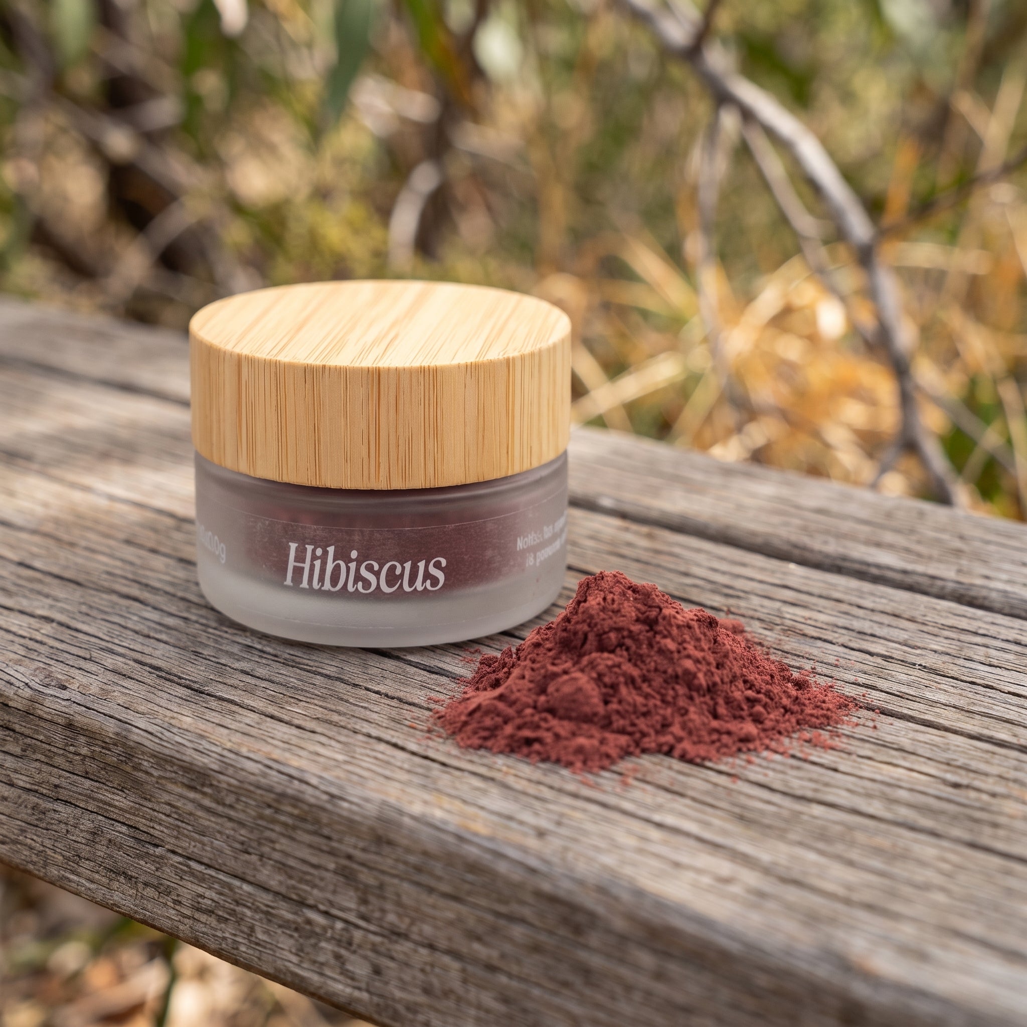 Jar of Eliézer Clay organic hibiscus powder with a mound of pink powder on a timber bench outdoors