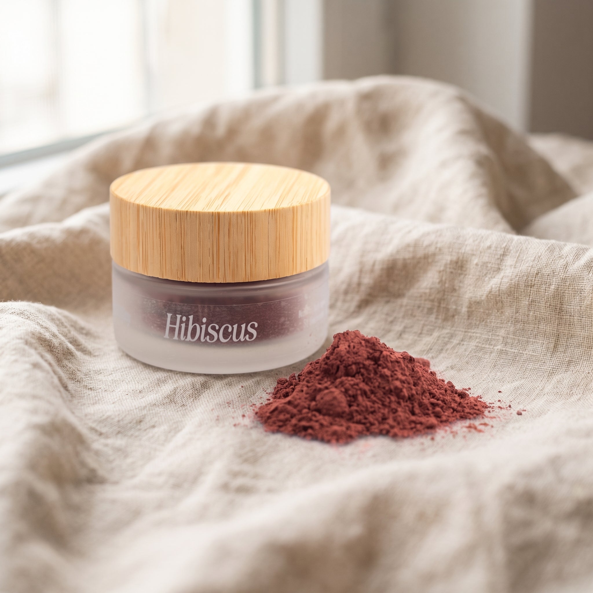 Jar of Eliézer Clay organic hibiscus powder with a mound of pink powder on natural linen